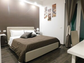 Quarto de hotel moderno com uma cama grande, mesas de cabeceira, uma escrivaninha e vista para a cidade.