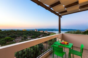 Un balcon avec une table et des chaises, donnant sur un paysage pittoresque, avec des arbres et des bâtiments.