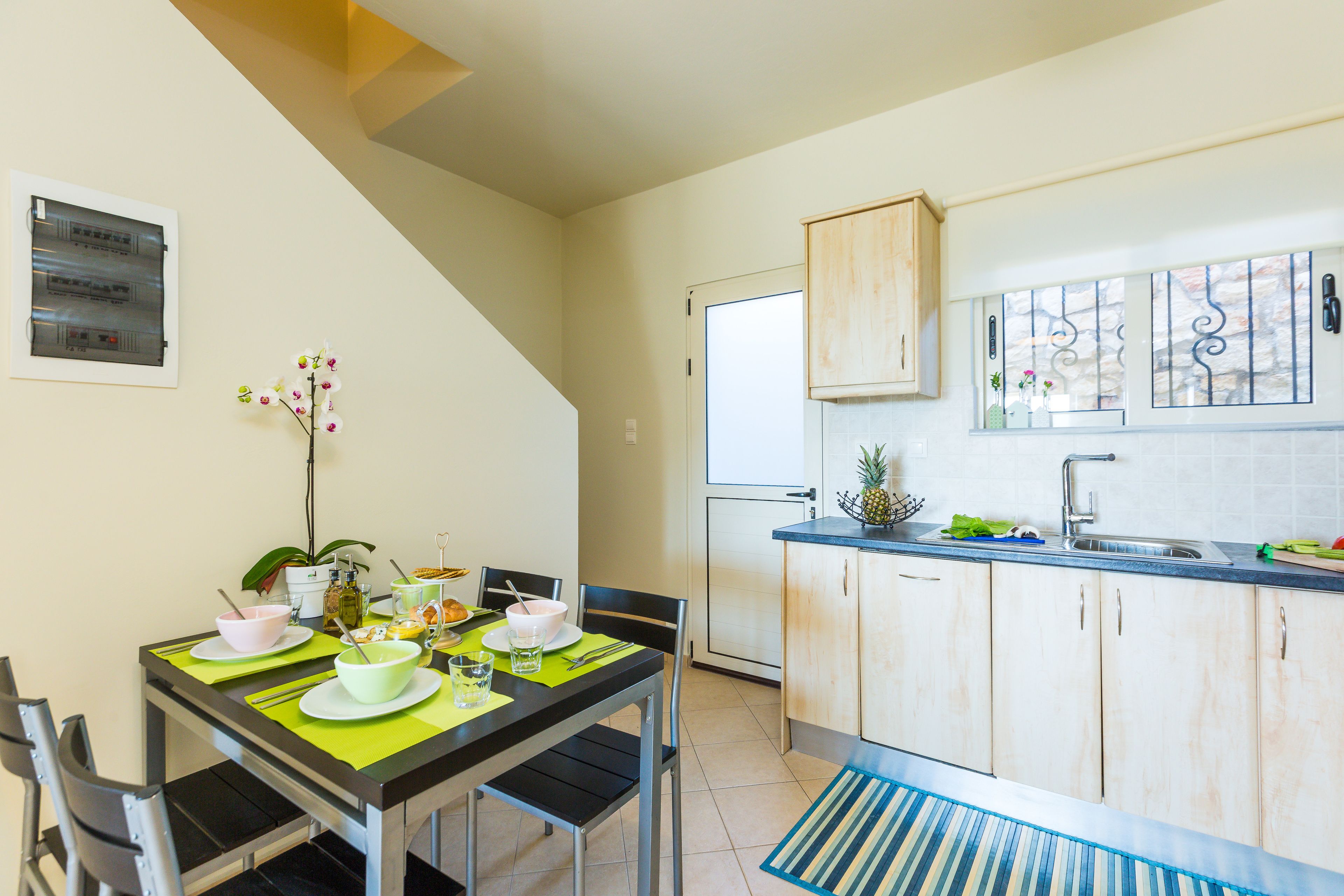 A compact kitchen with a dining area, featuring a dining table set with plates, bowls, and cutlery, and a small potted plant on the table.