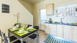 A compact kitchen with a dining area, featuring a dining table set with plates, bowls, and cutlery, and a small potted plant on the table. - Villa Alysso (Chania)