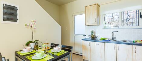 A compact kitchen with a dining area, featuring a dining table set with plates, bowls, and cutlery, and a small potted plant on the table.