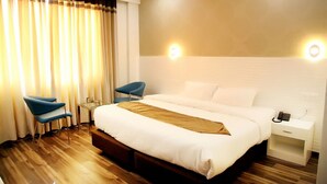 A hotel room with a large bed, two blue chairs, a bedside table with a lamp, and a phone on the nightstand. - Hotel Royal MJS Pinjore (Kalka)