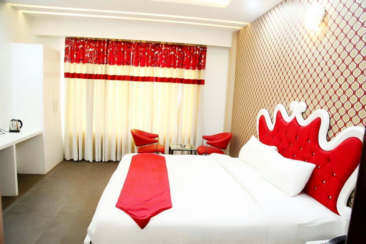 Une chambre d’hôtel avec un grand lit, deux fauteuils rouges, une petite table et un bureau.