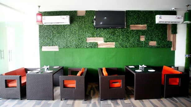 A room with a green artificial grass wall, air conditioning units, and wicker furniture with orange cushions. - Hotel Royal MJS Pinjore (Kalka)