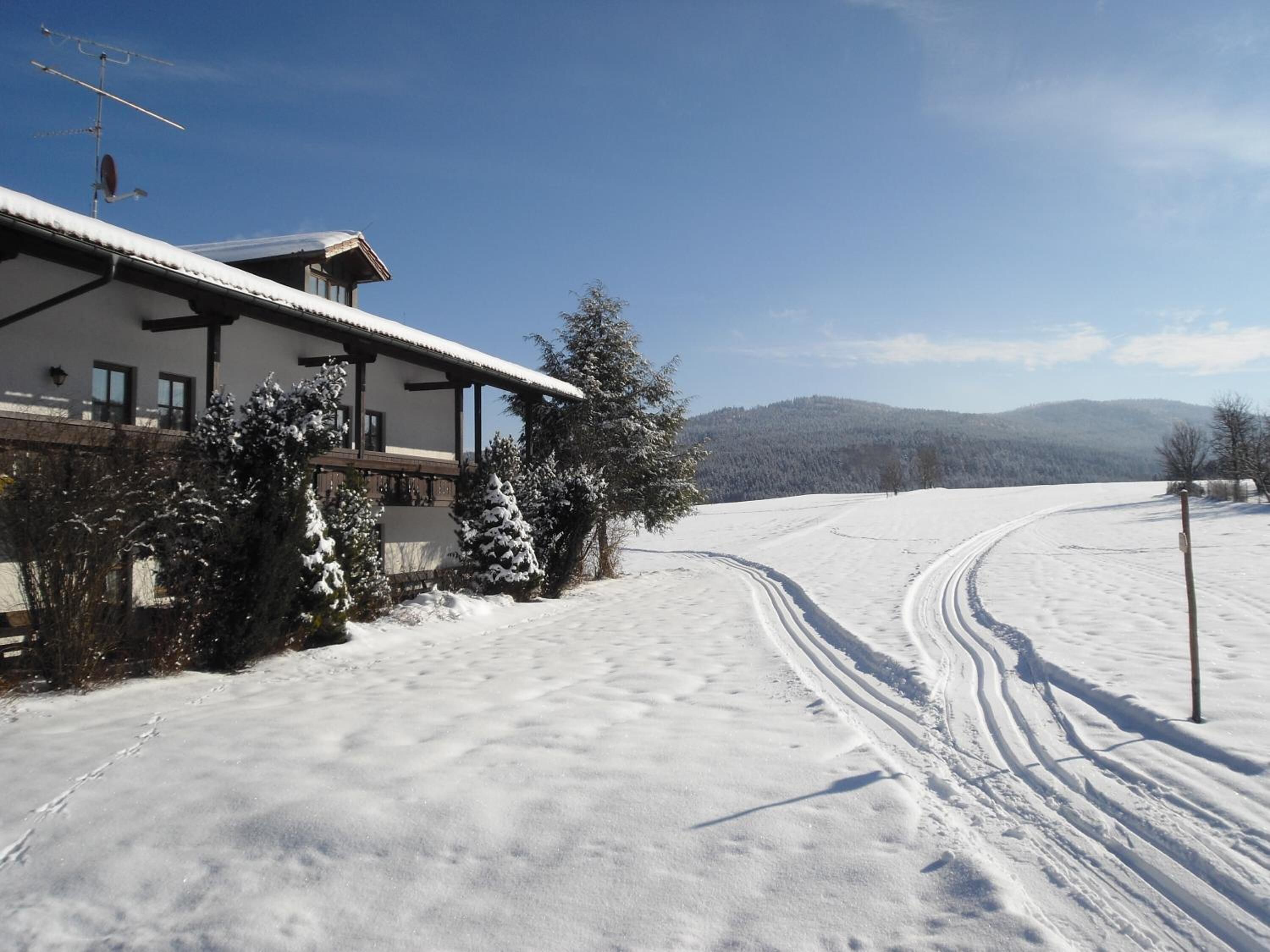 A snow-covered landscape with a house featuring a balcony and a ski slope.