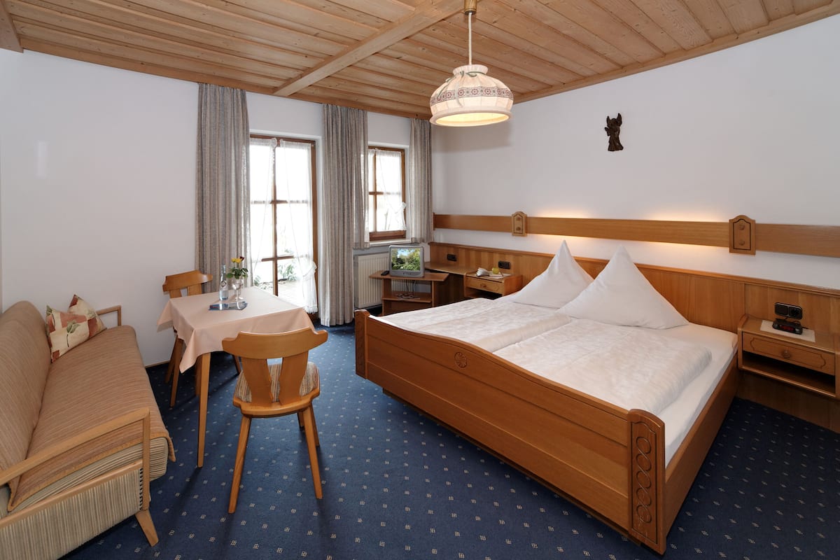 A hotel room with a wooden bed, a small table with chairs, a desk, and a window with curtains.