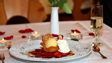 A dessert plate with strawberries, whipped cream, and a scoop of ice cream, accompanied by a glass of white wine and candles on a table.