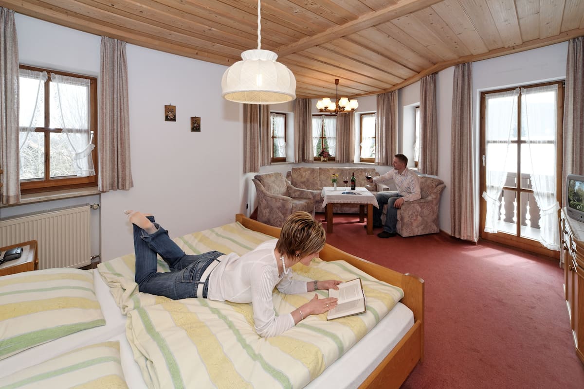 A bedroom with a bed, a sofa, a table with a bottle of wine, and a television.