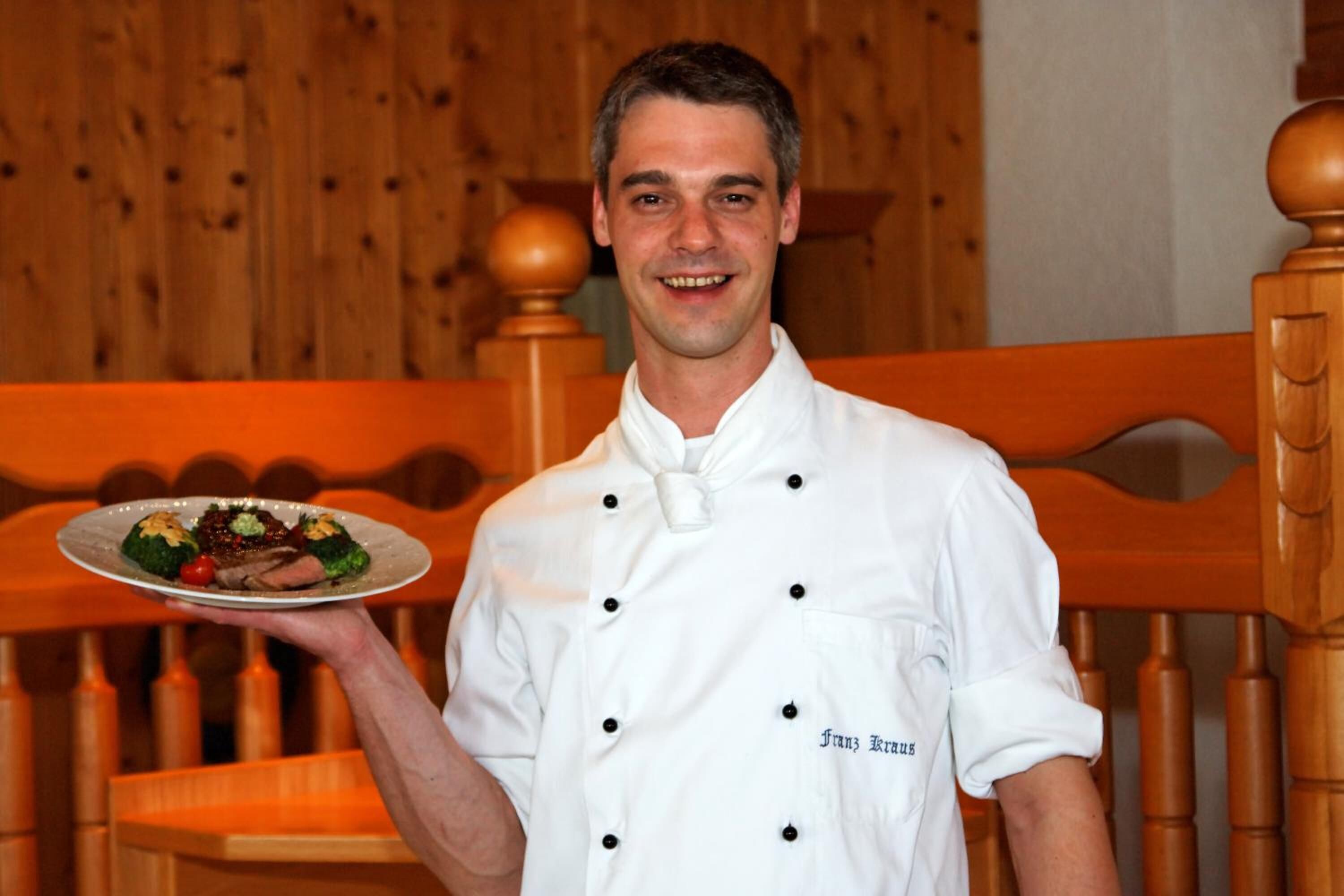 A person in a white chef's uniform holding a plate with food.