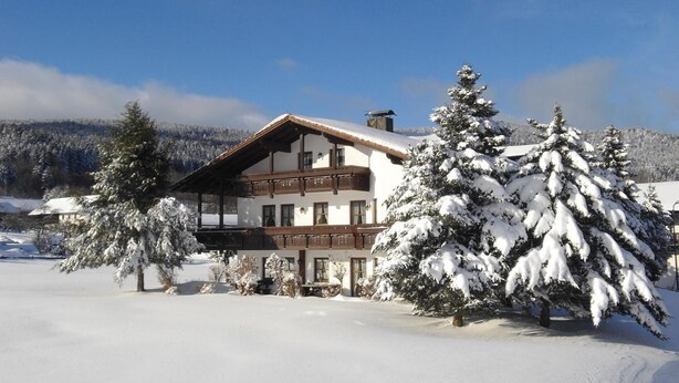 Un chalet à plusieurs étages doté d’un balcon, entouré d’arbres couverts de neige et avec une chaîne de montagnes en toile de fond.