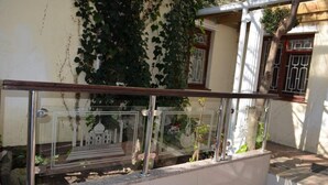 Une rambarde en verre offrant une vue sur un bâtiment dont les murs sont recouverts de lierre et une fenêtre ornée d’une grille métallique.
