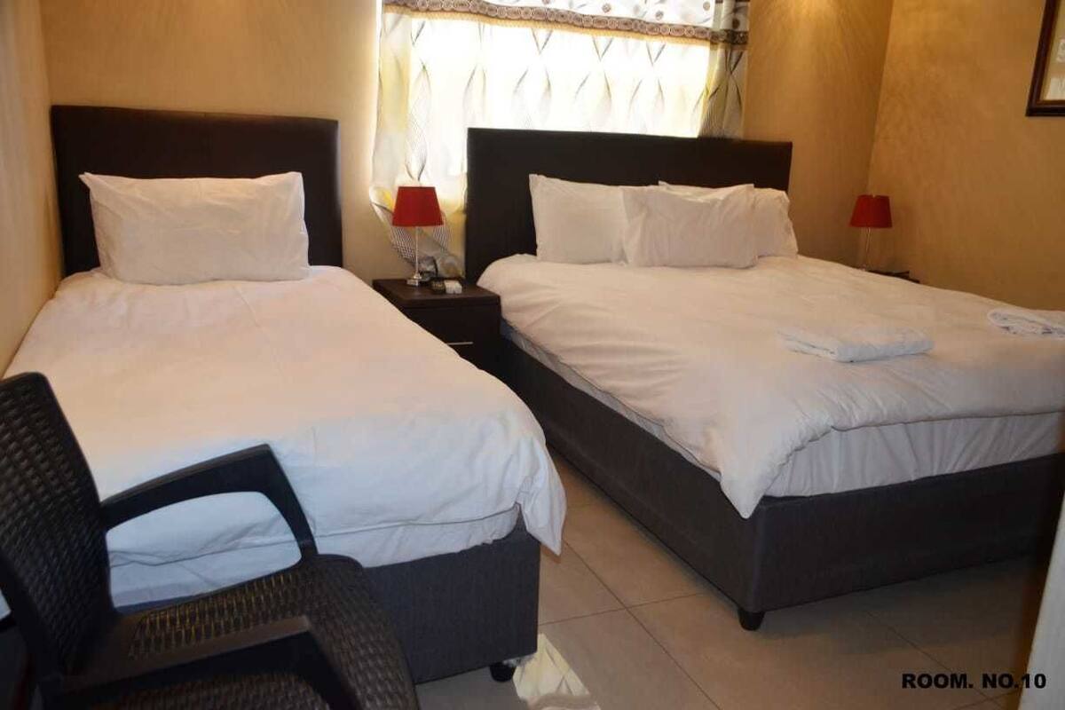 A hotel room with two beds, a chair, and two bedside tables with lamps.