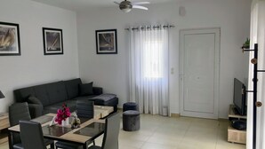 Ein modernes Wohnzimmer mit grauem Sofa, einem Esstisch mit Stühlen, einem Deckenventilator und einer Tür mit Vorhang.