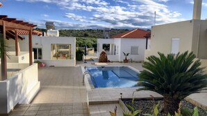 Ein moderner Poolbereich im Freien mit blauem Himmel, einer Pergola und Blick auf die umliegende Landschaft.