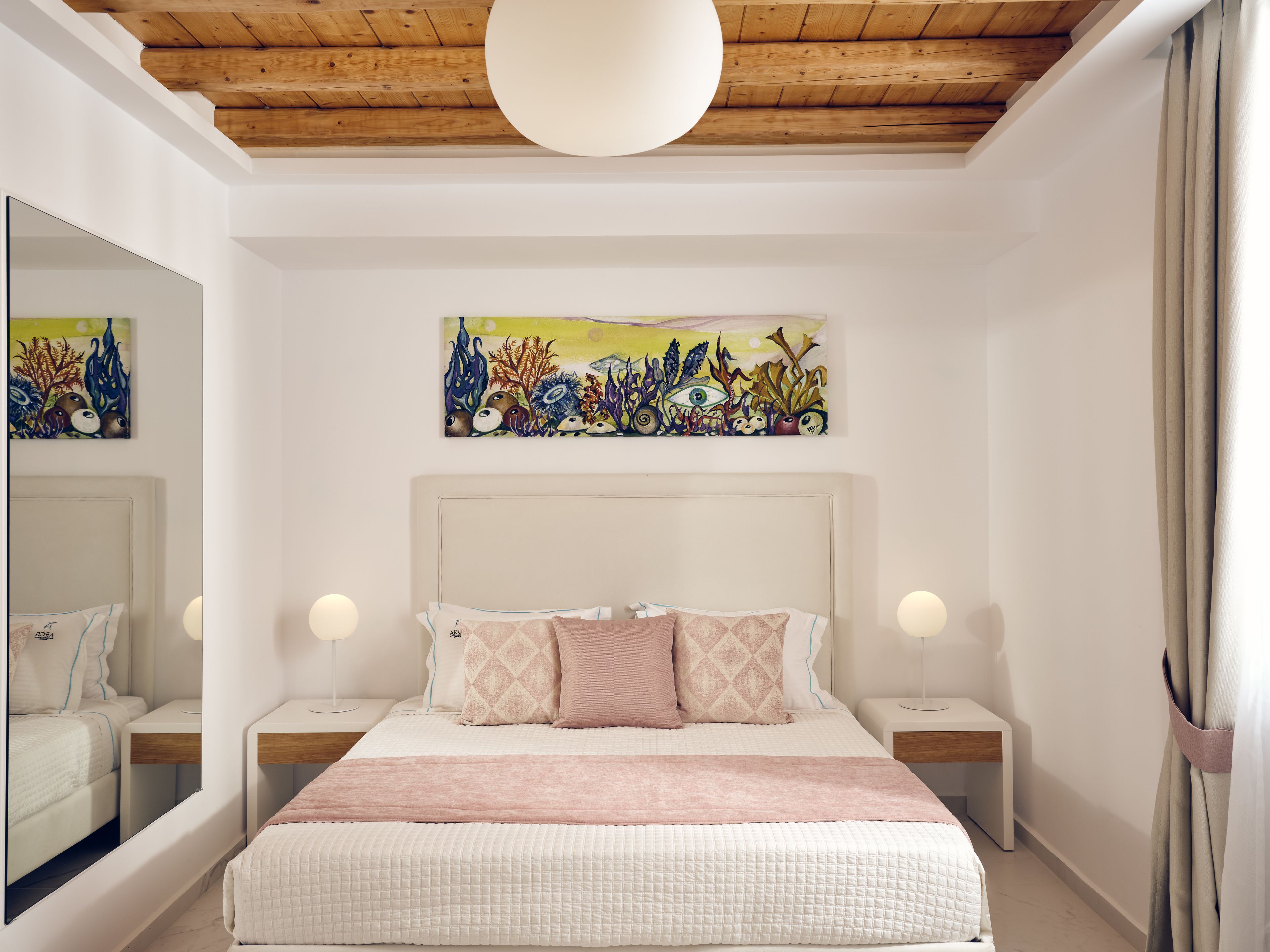 A bedroom with a bed, bedside tables, a mirror, and artwork on the wall.