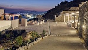 Une terrasse sur le toit offrant une vue sur une ville côtière au crépuscule, avec des murs en pierre et des sièges d’extérieur.