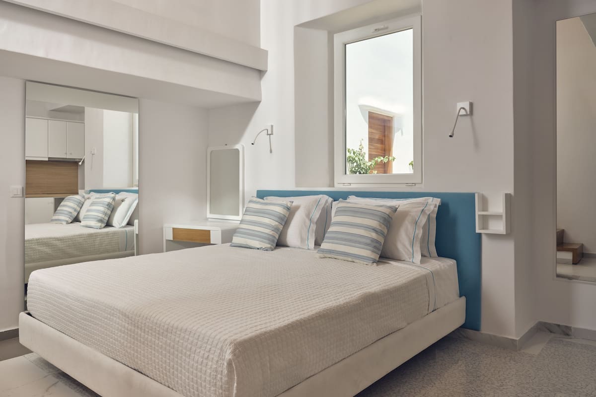 Un dormitorio moderno con una cama grande, un espejo, una ventana y una mesita de noche.
