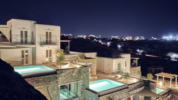 Une villa moderne dotée de plusieurs piscines, de murs en pierre et offrant une vue sur le paysage environnant la nuit.