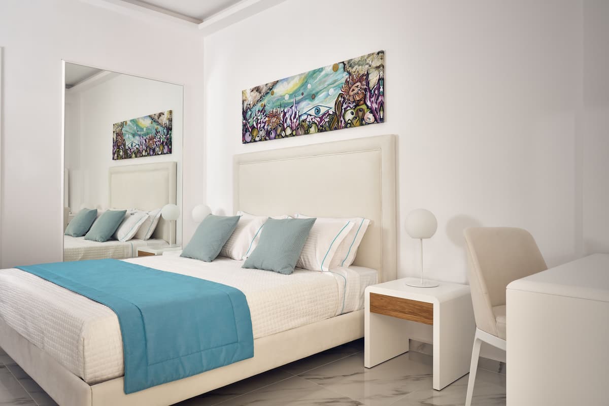 Un dormitorio moderno con una cama grande, una mesita de noche, una silla y dos obras de arte colgadas en la pared.