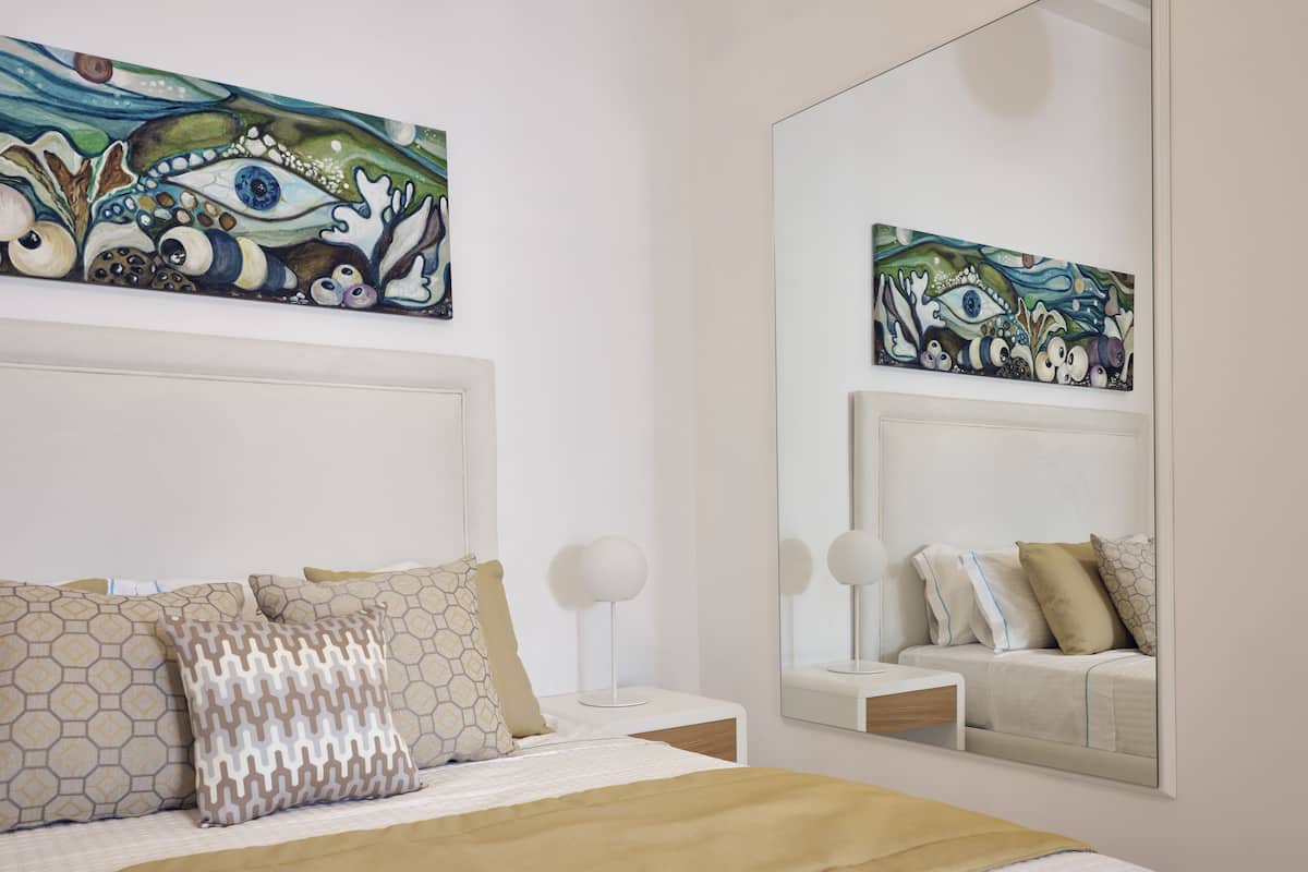Un dormitorio moderno con una cama grande, almohadones estampados, una mesita de noche, un espejo y un cuadro en la pared.