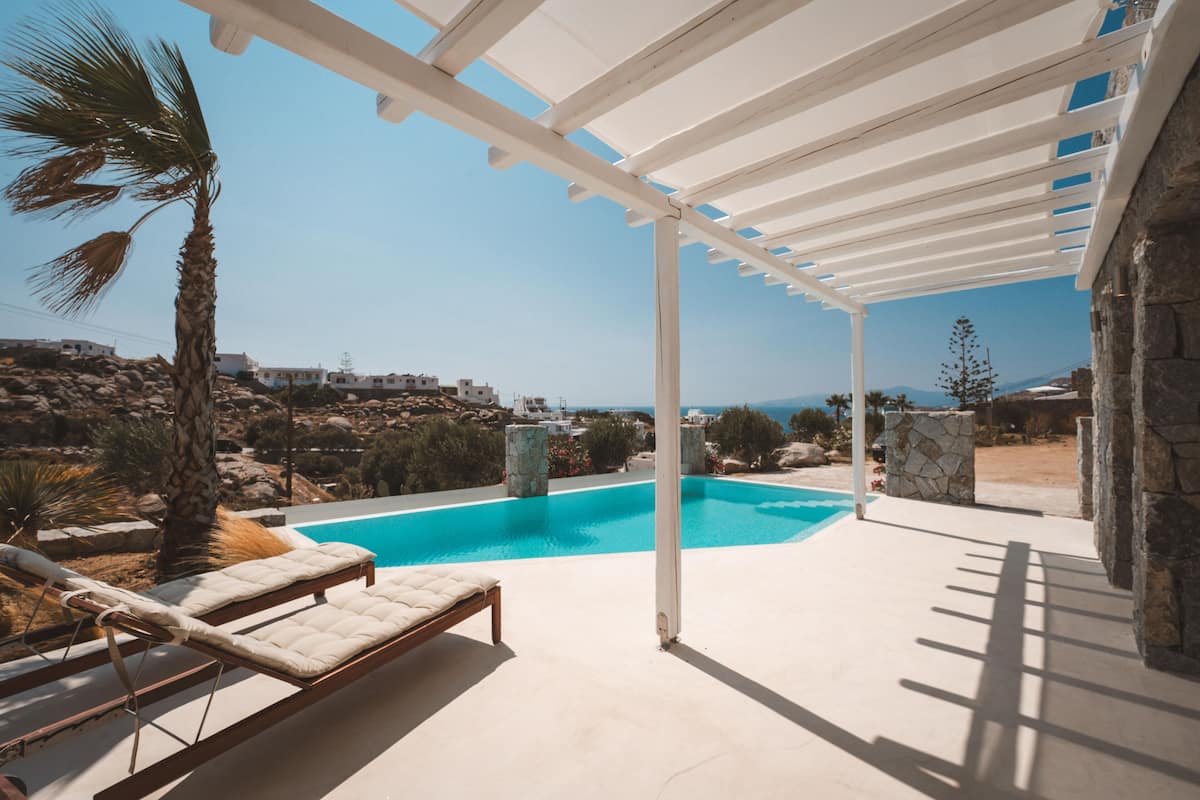 Un espacio al aire libre techado con piscina, sillas de descanso y vistas del paisaje circundante.