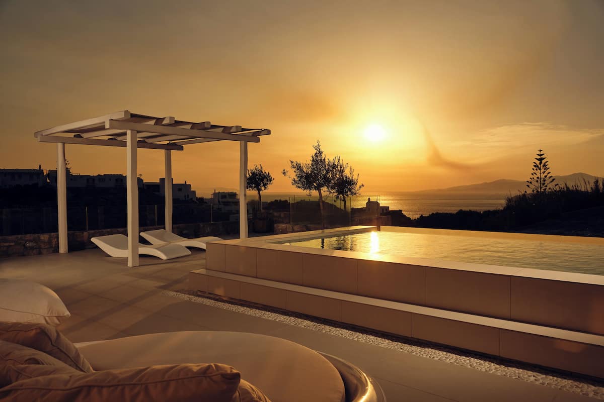 Zona de piscina exterior moderna con sillones de descanso y una pérgola, con vistas a un hermoso atardecer.