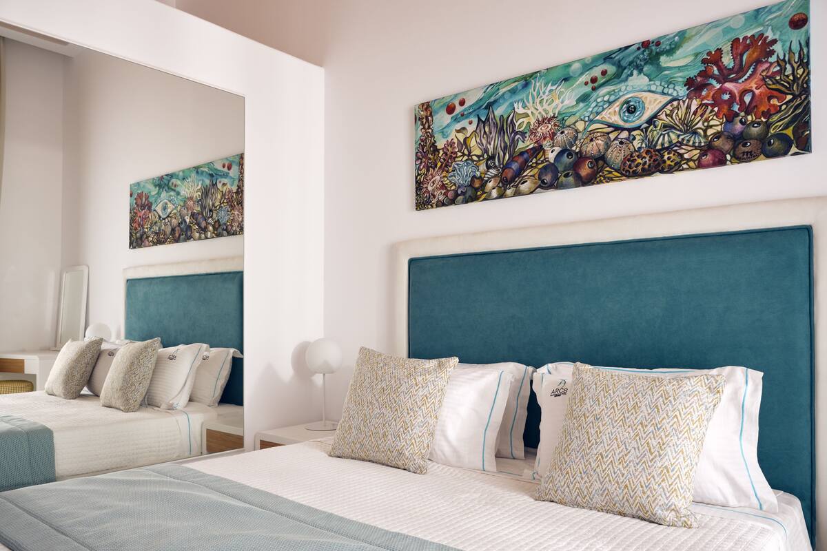 Habitación de hotel con dos camas, cabecero color aguamarina y un cuadro de gran tamaño con temática marina sobre las camas.