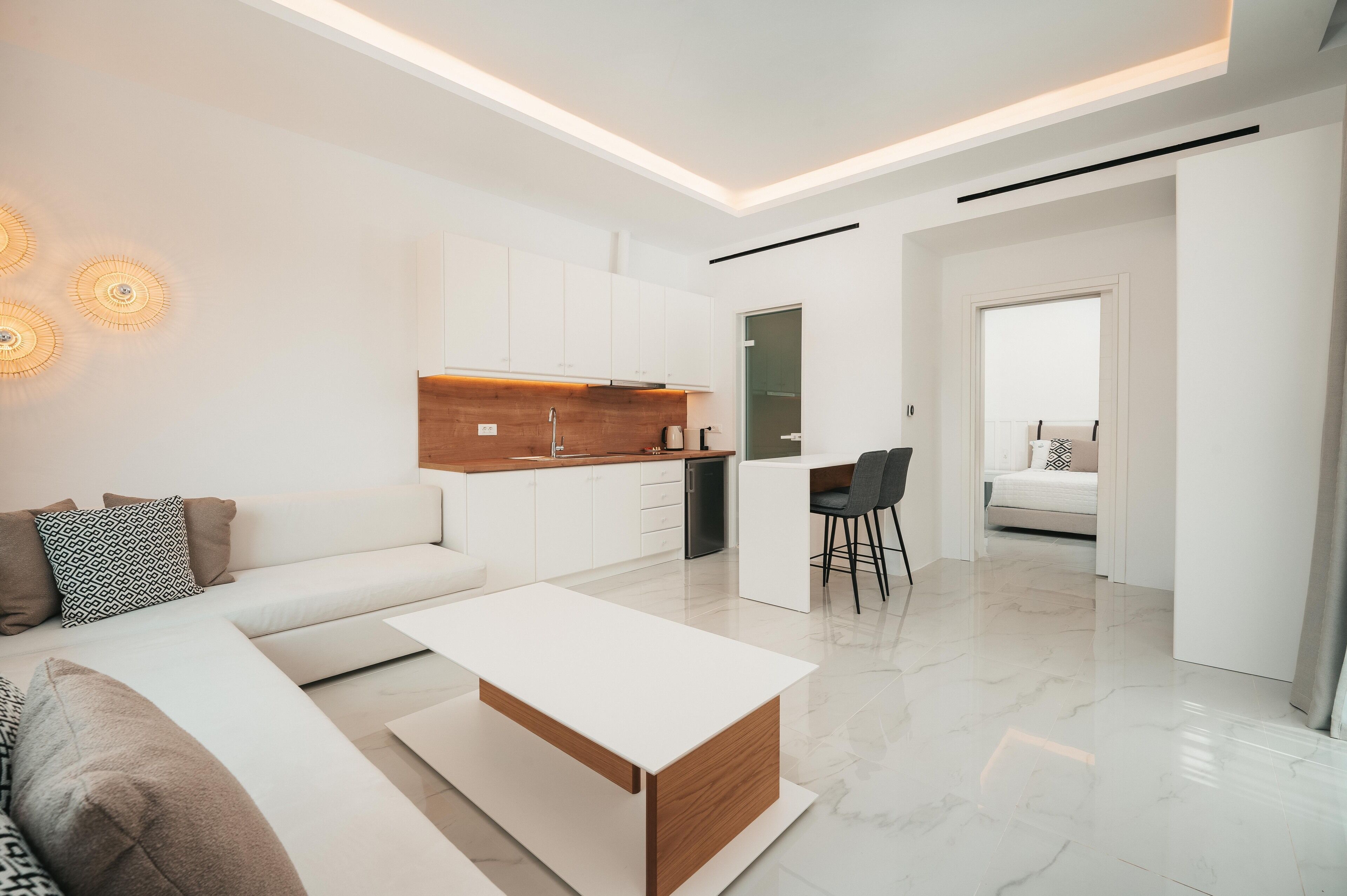 A modern living room with a white sofa, a coffee table, and a kitchen area with white cabinets and a wooden countertop.