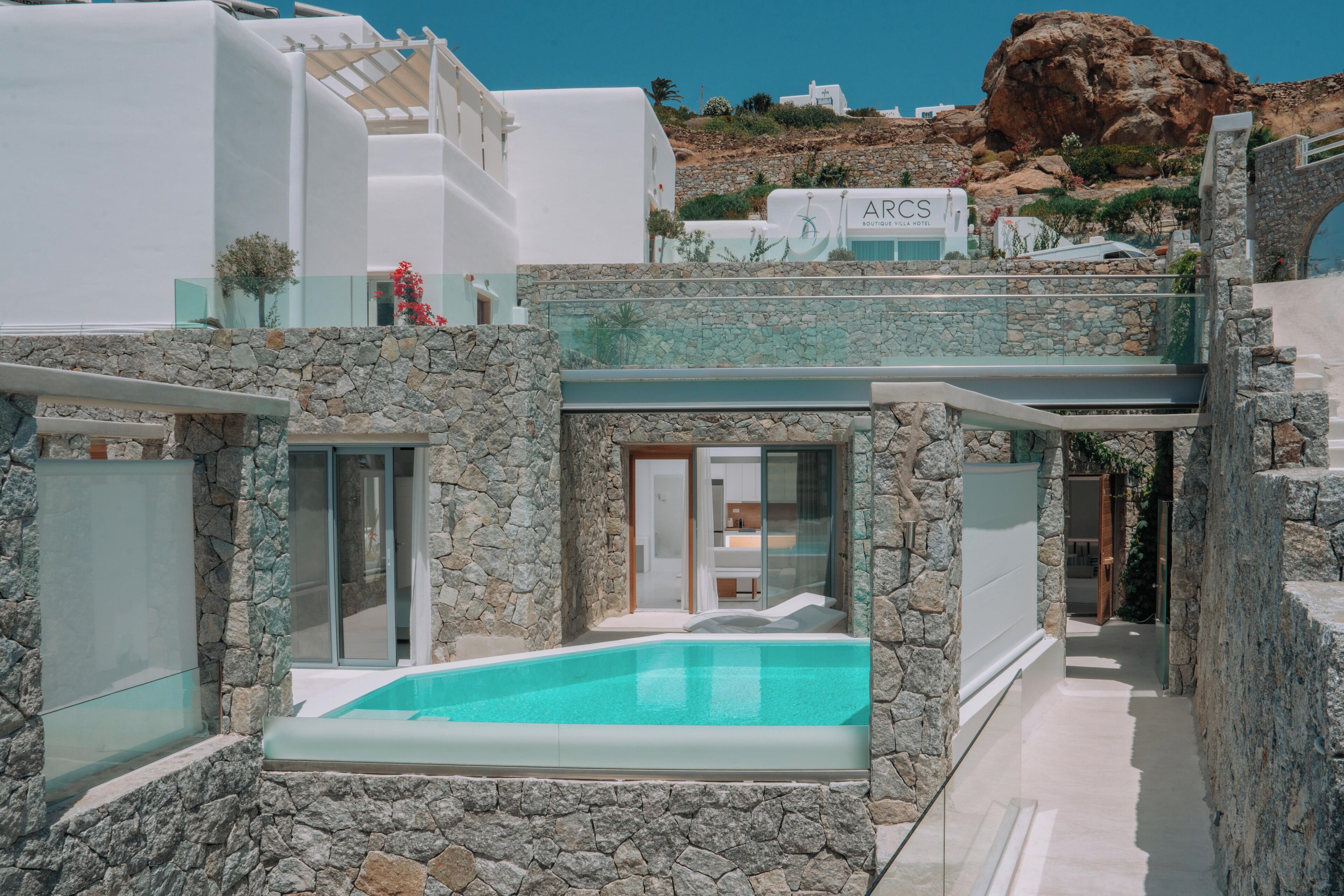 A modern villa with a stone exterior, a swimming pool, and a view of a rocky hillside.