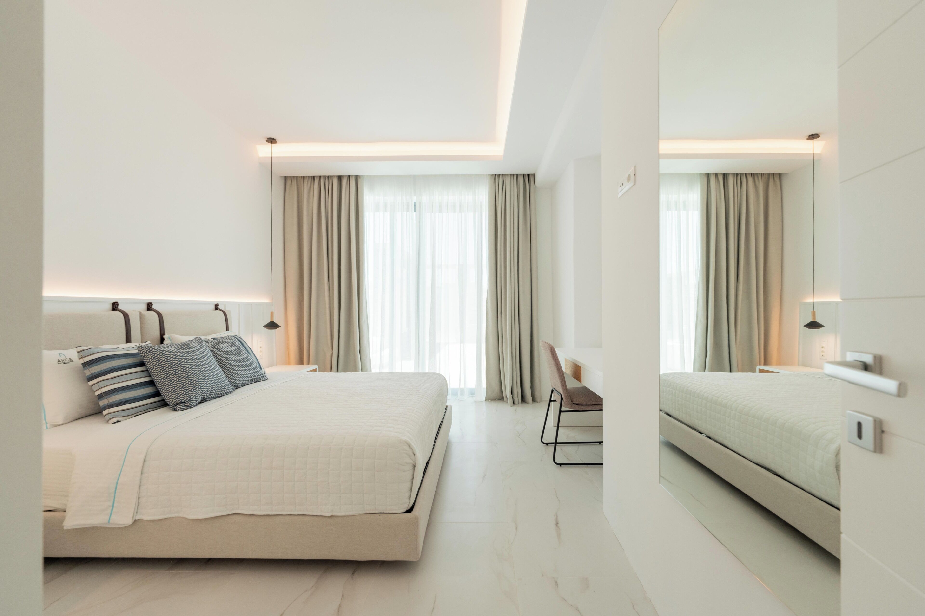 Una habitación de hotel moderna con una cama grande, mesitas de noche, una silla y un espejo.