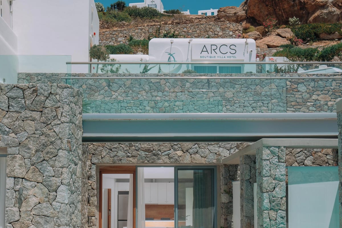 Una villa moderna con fachada de piedra, piscina y vistas del paisaje circundante.