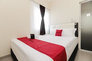 Ein Hotelzimmer mit einem Bett, einer rot-weißen Tagesdecke, einer schwarzen Tasche und einem roten Kopfkissen.