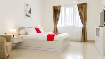 A hotel room with a bed, a nightstand, a lamp, a TV, and a window with curtains.