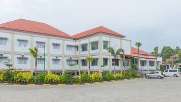 A multi-story hotel with a red roof, white exterior walls, and a paved courtyard with plants and a car.