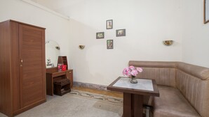 A bedroom with a wooden wardrobe, a desk with a vase of flowers, a brown leather sofa, and a wall with framed pictures. - RedDoorz @ Lawang (Malang)
