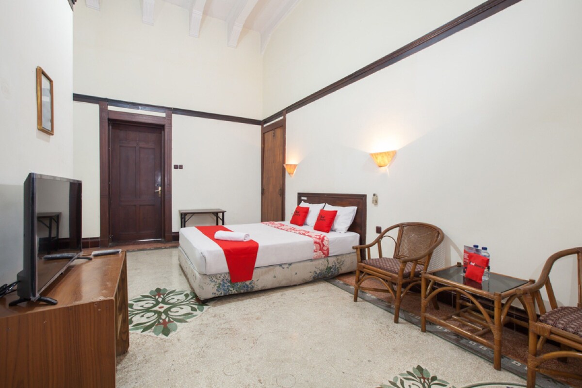 A hotel room with a bed, two chairs, a small table, a TV, and a door.