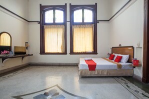 A hotel room with a bed, a desk, and two windows with curtains.
