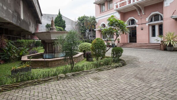 A courtyard with a fountain, potted plants, and a building with a pink facade and balconies. - RedDoorz @ Lawang (Malang)