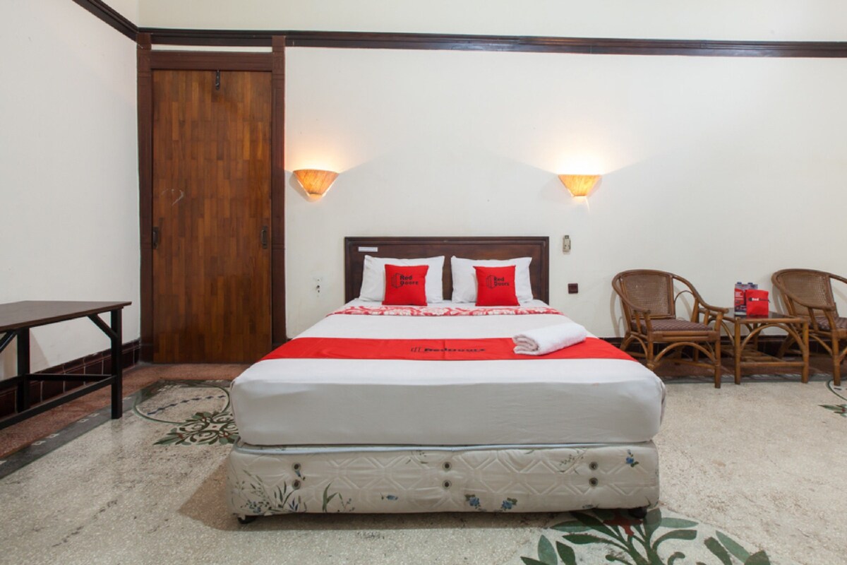 A neatly arranged hotel room with a bed, two chairs, a table, and a wooden door.