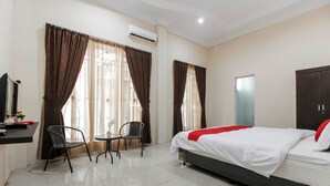 A hotel room with a bed, a desk with a chair, a small table, and a wardrobe. - RedDoorz near Grand Palladium (Medan)