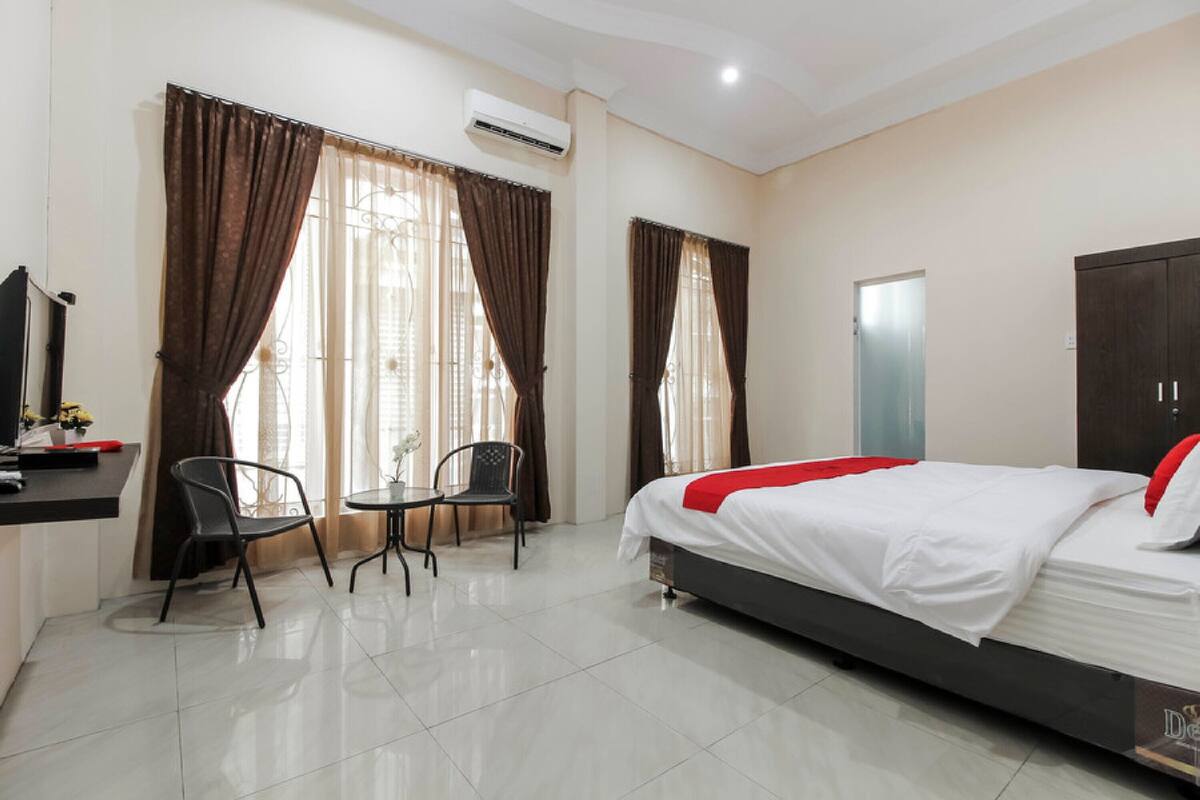 A hotel room with a bed, a desk with a chair, a small table, and a wardrobe.