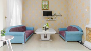 A living room with two blue sofas, a white coffee table, a flat-screen TV, and a patterned wallpaper. - RedDoorz near Grand Palladium (Medan)