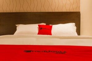 A hotel bed with a white and red bedspread, a wooden headboard, and a red pillow with the RedDoorz logo. - RedDoorz Plus @ Dipatiukur (Bandung)