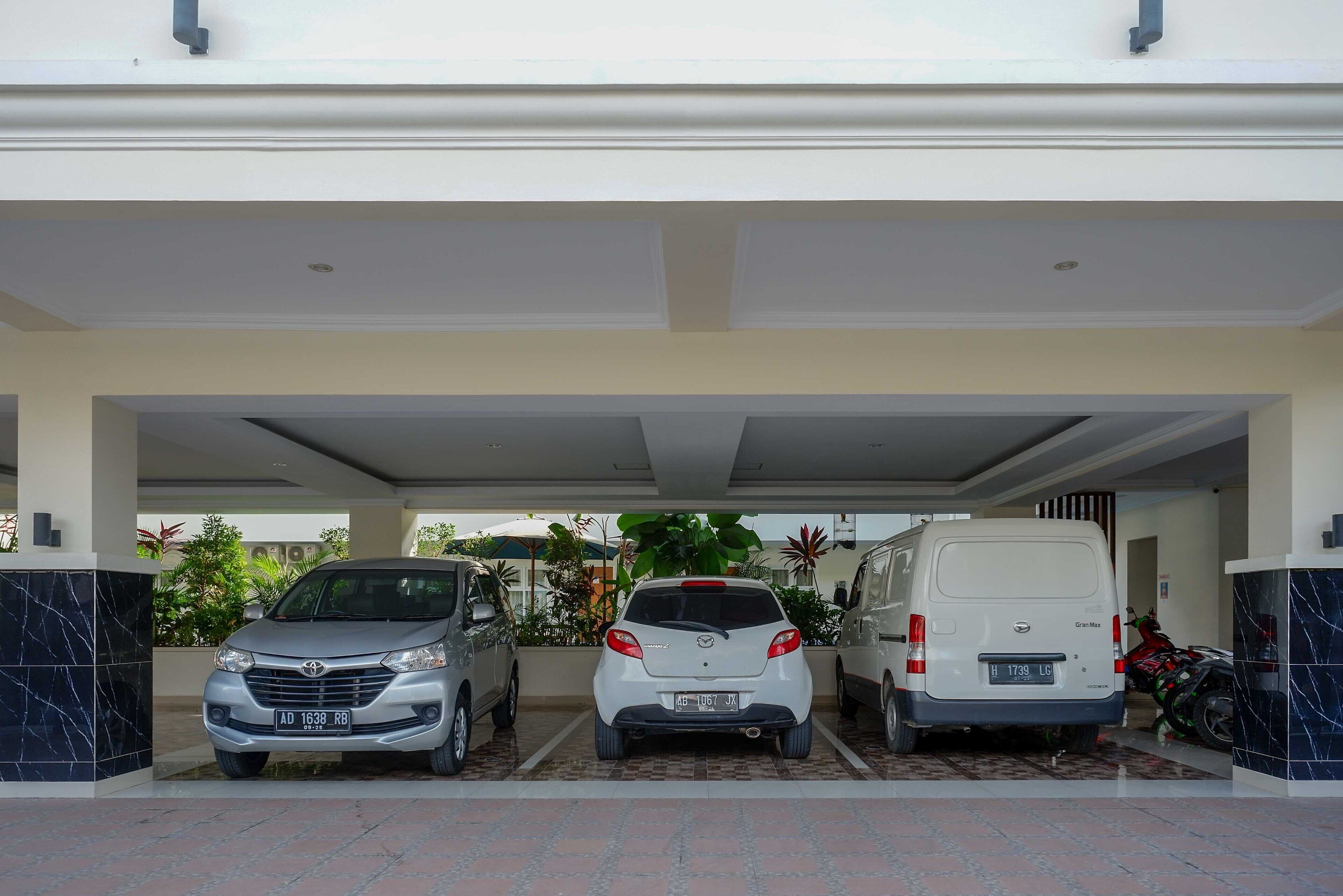 A covered parking area with three vehicles: a silver SUV, a white hatchback, and a white van.