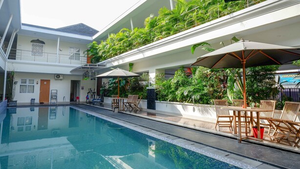 A swimming pool with a sun terrace, outdoor seating, and lush greenery. - Urbanview Hotel Syariah Casa Azmya Yogyakarta (Depok)