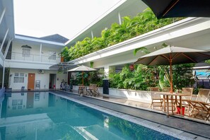 Une piscine dotée d’une terrasse ensoleillée, d’un espace salon extérieur et d’une végétation luxuriante.