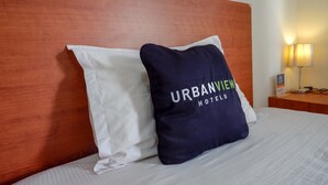 A hotel room with a wooden headboard, a white pillow, and a navy pillow with "URBANVIEW HOTELS" text. - Urbanview Hotel Syariah Casa Azmya Yogyakarta (Depok)