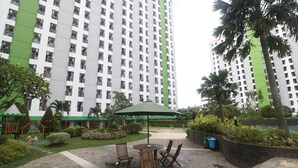 A courtyard with a table and chairs, surrounded by greenery and a high-rise building in the background. - RedLiving Apartemen Green Lake View Ciputat - Pelangi Rooms Tower E (South Tangerang)