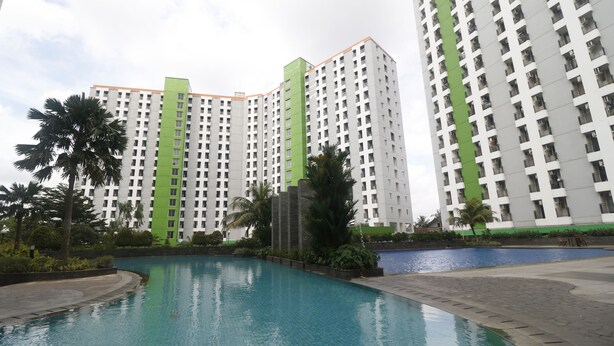 A modern hotel with a pool area, surrounded by high-rise buildings and palm trees. - RedLiving Apartemen Green Lake View Ciputat - Pelangi Rooms Tower E (South Tangerang)