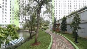 A landscaped pathway with a brick border, a small pond, and a building with a green facade in the background. - RedLiving Apartemen Green Lake View Ciputat - Pelangi Rooms Tower E (South Tangerang)
